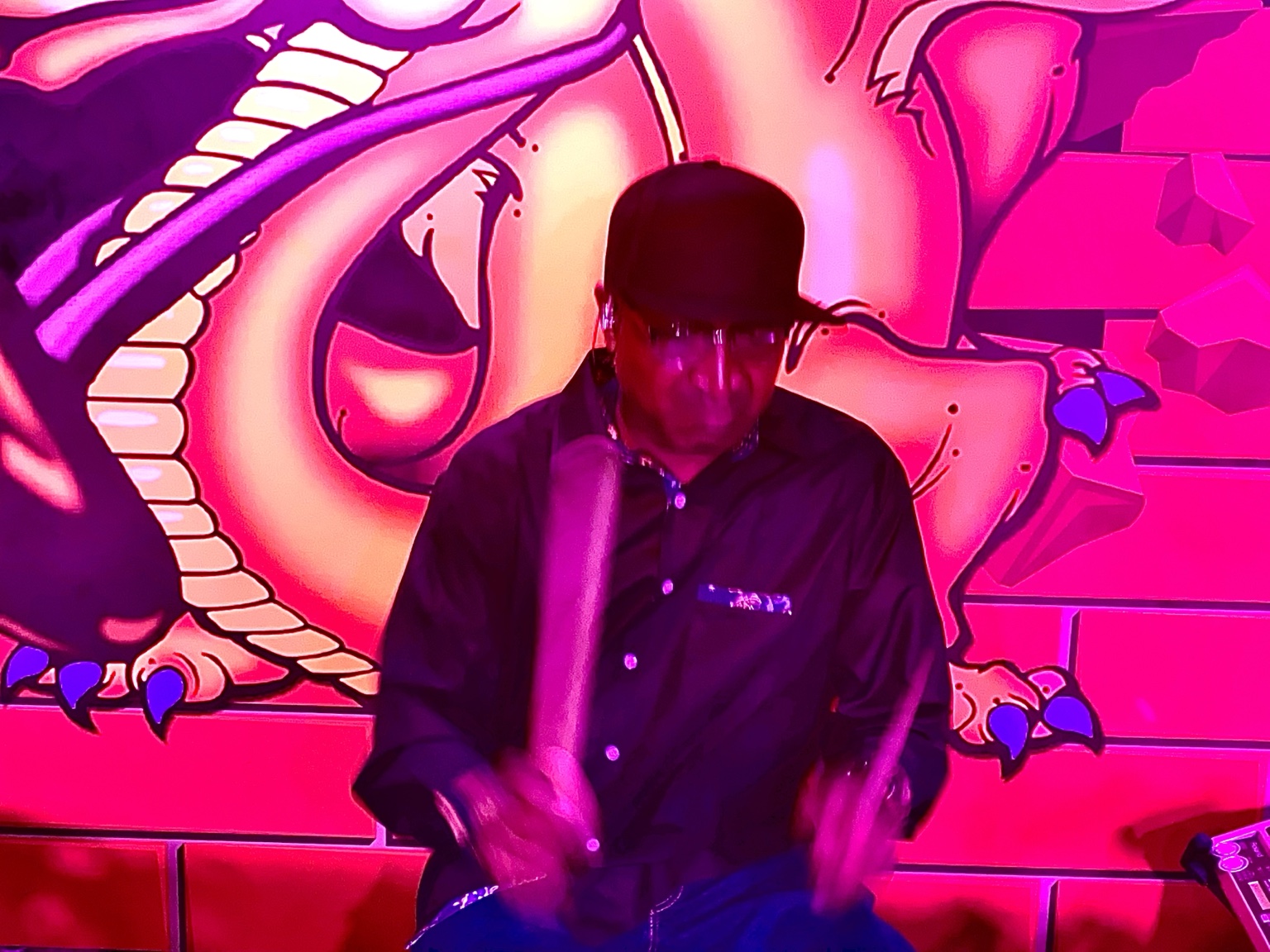 SWITCH drummer performing under vivid pink and purple lights in front of a dragon mural